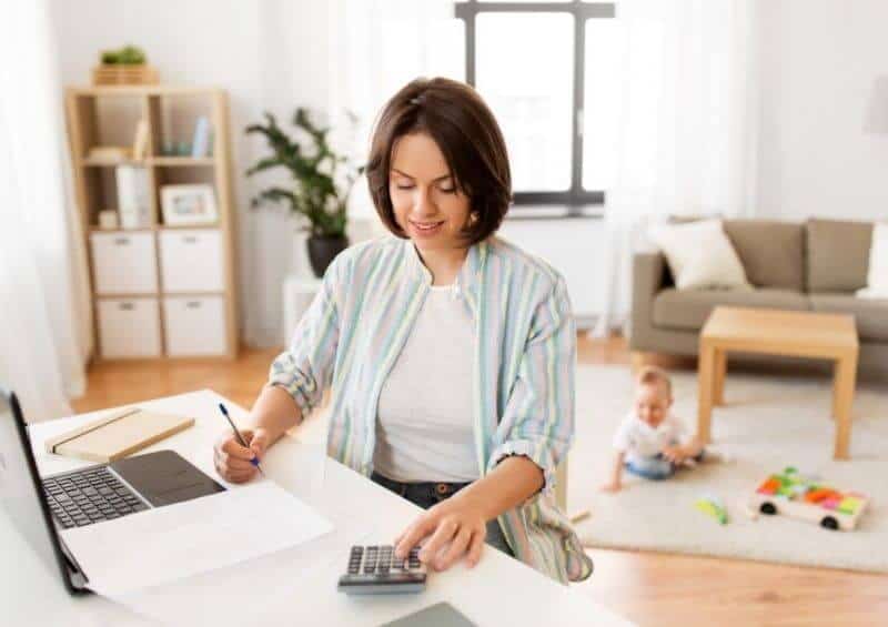 mom working from home writing on paper and using a calculator