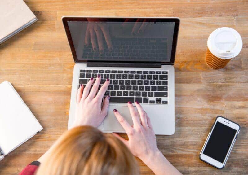 woman working from home on a laptop with coffee cup and phone on table