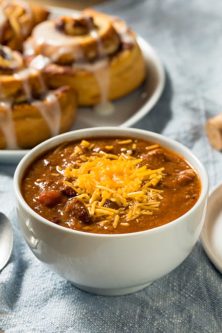 Chili soup served in a white bowl next to two cinnamon rolls on a plate