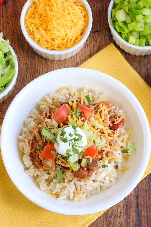 Table set with chicken burrito bowl recipe and toppings in white serving dishes.