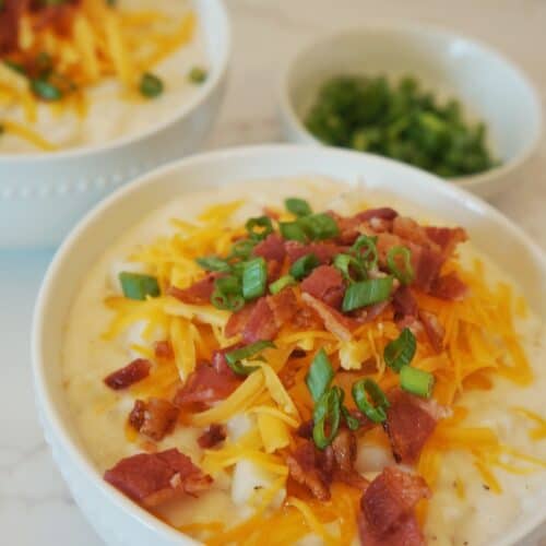 slow cooker potato soup served on a whihte bowl and topped with bacon, cheese, and parley.