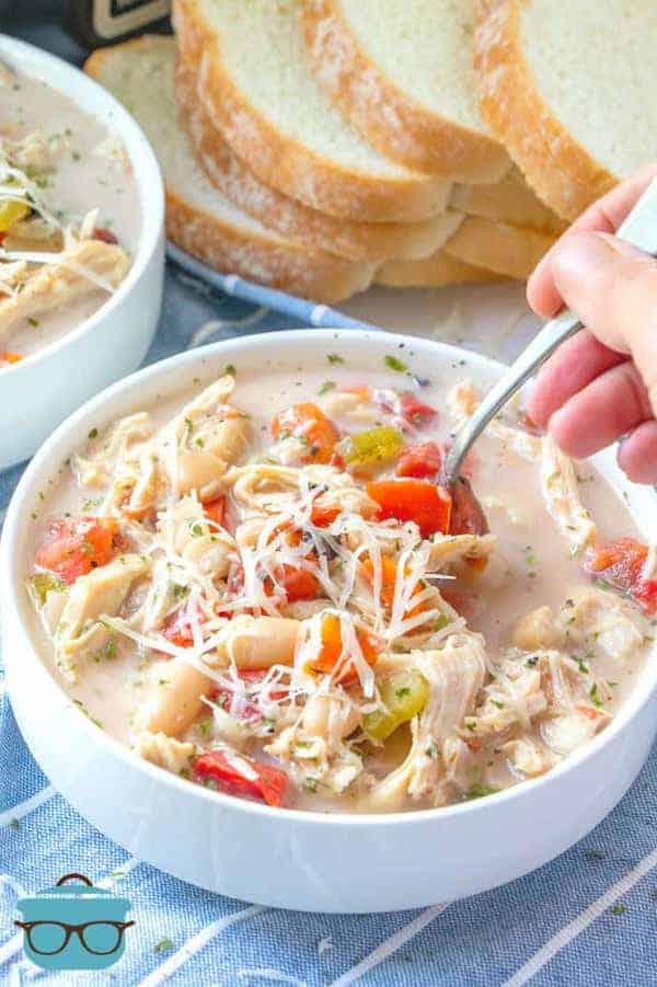 Slow Cooker Creamy Tuscan Chicken Soup served in a white bowl and a hand stirring the soup with a spoon.