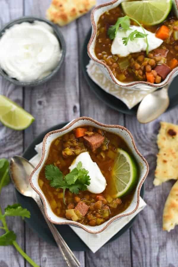 Two bowls of lentil soup, with naan bread, lime wedges and yogurt.