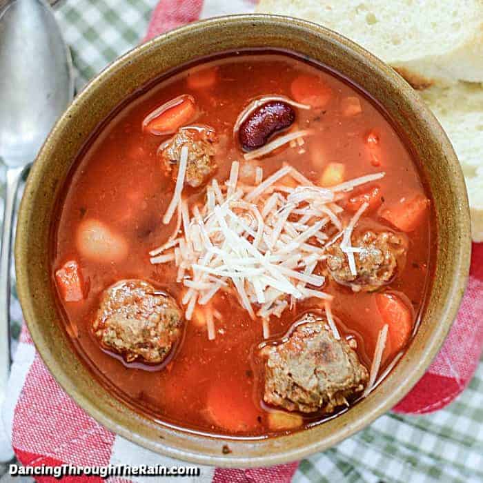 Slow Cooker Meatball Soup in a brown bowl next to a metal spoon on a red and white napkin and two slices of Italian bread