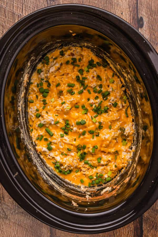 Prepared crack chicken garnished with chives  inside a black crock pot