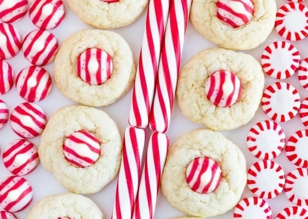 Red-and-white candy cane cookies topped with a candy-cane-flavored Hershey’s Kiss and sprinkled with crushed peppermint, arranged on a holiday platter.