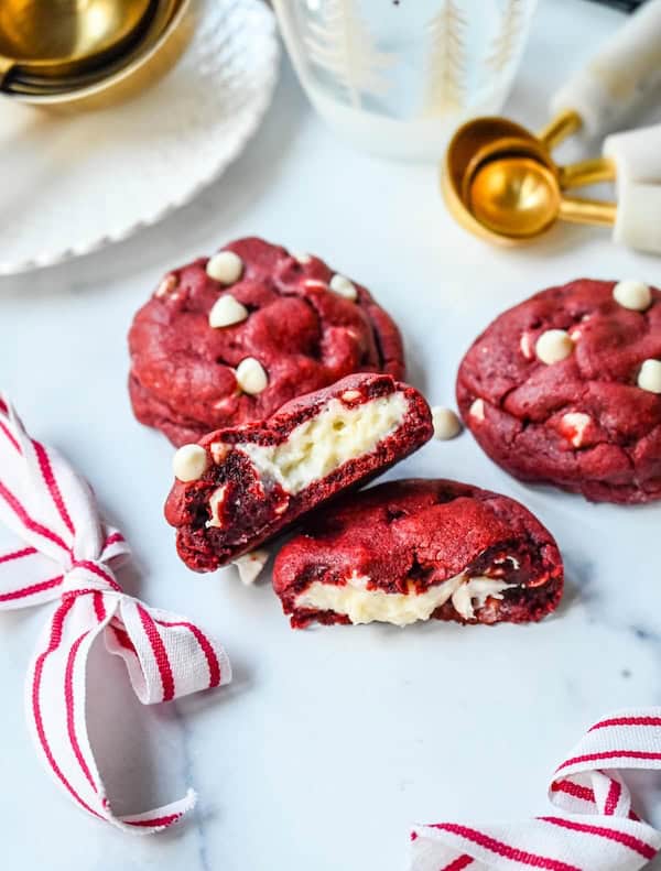 Red velvet cookies stuffed with creamy cheesecake filling and dotted with white chocolate chips, displayed on a Christmas cookie tray for a festive holiday dessert.