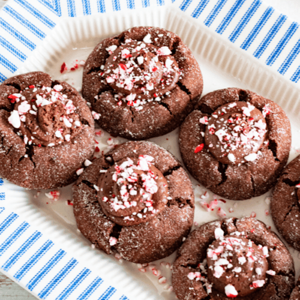 Chocolate thumbprint cookies with peppermint chocolate filling and crushed candy-cane topping, neatly arranged on a holiday cookie platter.