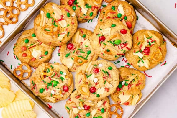 Big chewy Christmas cookies loaded with red-and-green M&Ms, pretzel pieces, potato chips and white chocolate chunks on a wooden board — homemade budget-friendly holiday cookie mixture.