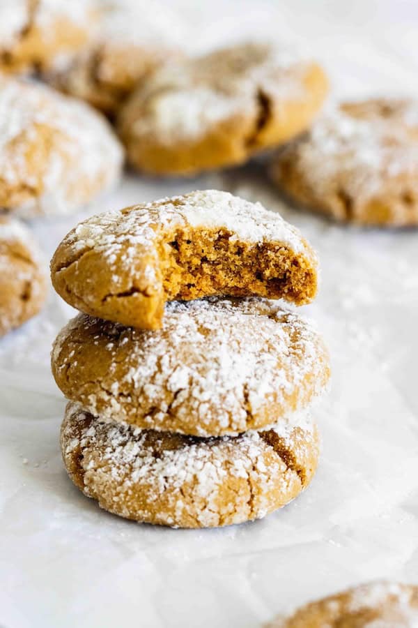 Chewy gingerbread crinkle cookies rolled in powdered sugar with crackled tops, festive homemade holiday cookies on a Christmas tray.