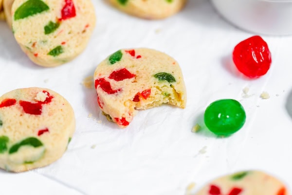 Cream-colored ice-box cookies flecked with red and green maraschino cherries, sliced from dough logs on a rustic holiday platter — budget-friendly classic Christmas cookie flavors.