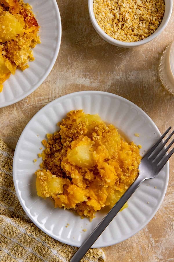 Serving of pineapple cheese casserole on a round white plate with fork — a make-ahead Christmas side dish.
