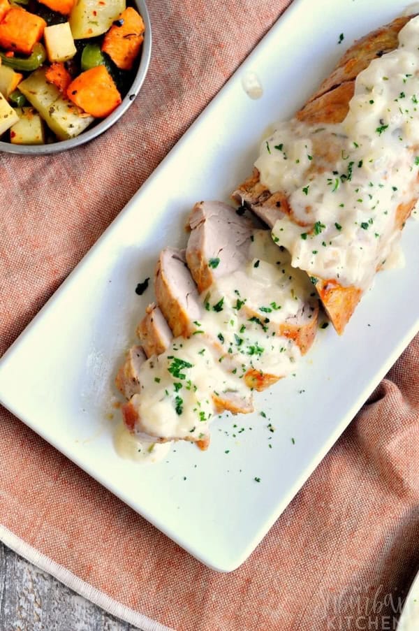 Roasted pork tenderloin sliced and topped with creamy white wine sauce for a Christmas dinner.