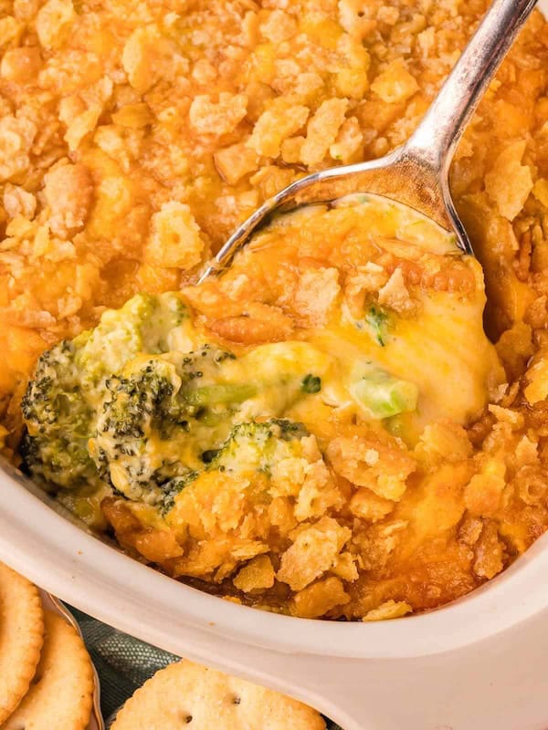 Cheesy broccoli casserole topped with crushed butter cracker crumbs in a white baking dish with a spoon — a make-ahead Christmas side dish.