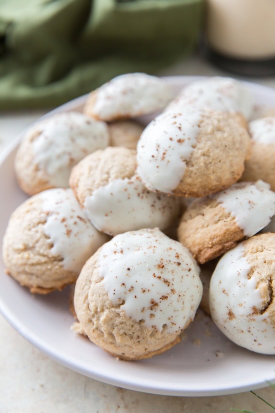 Soft eggnog sugar cookies dipped halfway in white chocolate on a holiday platter — homemade budget-friendly Christmas cookie flavors.