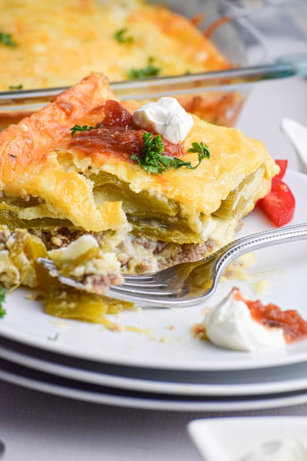Slice of chile relleno breakfast casserole on a white plate with a fork, topped with sour cream and salsa — a make-ahead Christmas breakfast.