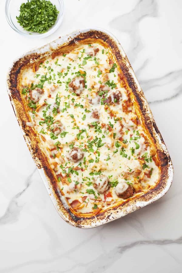 Cheesy meatball pasta casserole in a baking dish topped with melted mozzarella — a make-ahead Christmas dinner casserole.