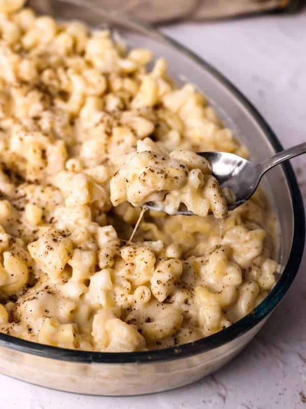 Creamy white cheddar mac and cheese served in a white baking dish with a spoon — an easy make-ahead Christmas dinner casserole.