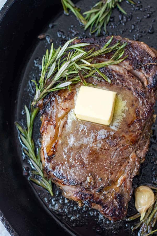 Boneless ribeye steak seared in a cast-iron pan with a sprig of rosemary for a festive Christmas meal.