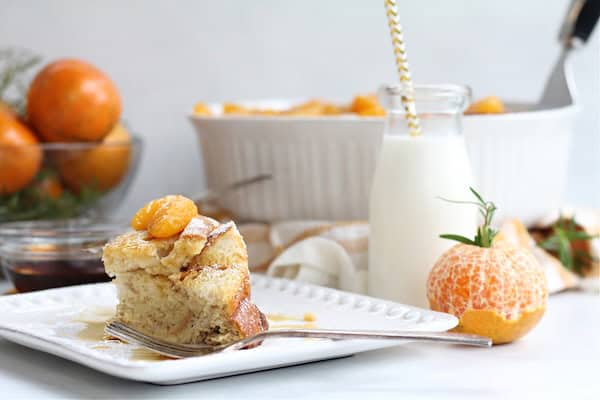 Slice of tangerine French toast casserole on a white plate with a fork, topped with tangerine slices — a cozy make-ahead Christmas breakfast.
