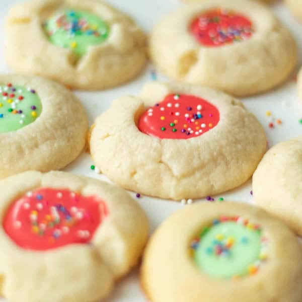 Shortbread thumbprint cookies filled with glossy icing and sprinkled with red and green bits, arranged on a holiday platter for Christmas cookie trays.