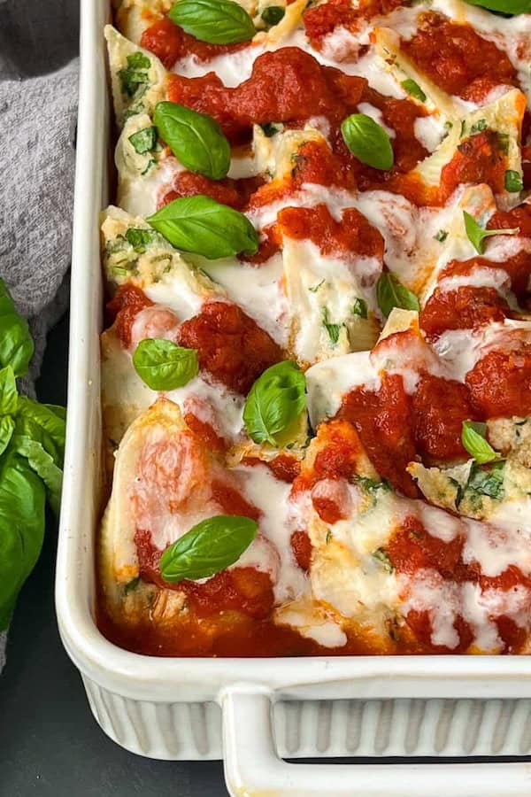 Baking dish of vegan stuffed pasta shells with marinara sauce and dairy-free cheese garnished with fresh herbs for Christmas dinner.