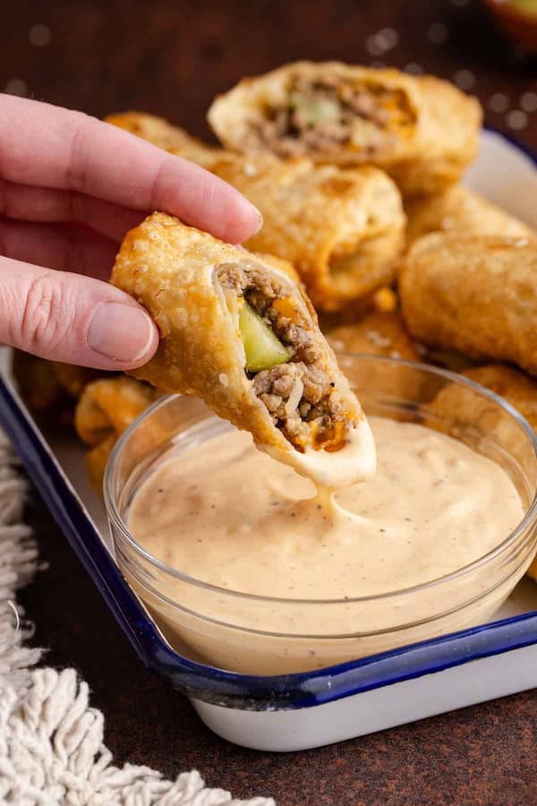 Golden Big Mac egg rolls stacked on a plate with dipping sauce on the side.
