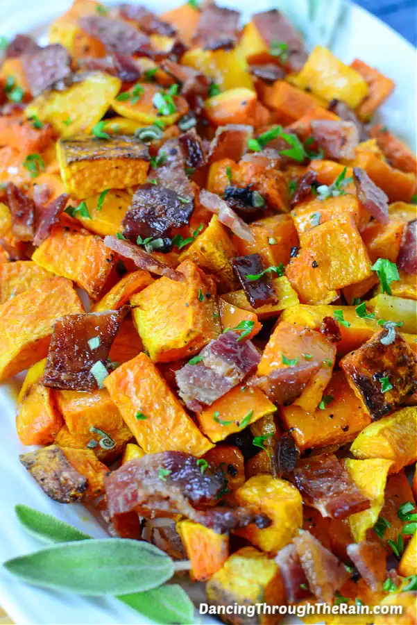 Roasted butternut squash cubes with bacon and sage on a white platter — flavorful easy Christmas side dish.