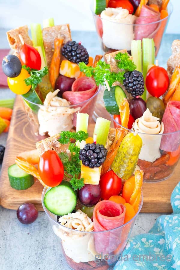 Mini charcuterie cups filled with cheese, meats, and fruit on a Christmas serving board.