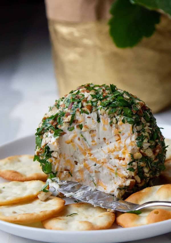 Round festive cheese ball rolled in herbs and nuts with crackers on a Christmas platter.