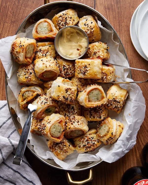 Flaky puff pastry sausage rolls on a holiday serving tray with dipping sauce.