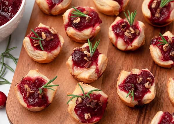 Golden cranberry brie bites baked in puff pastry cups and topped with fresh rosemary.