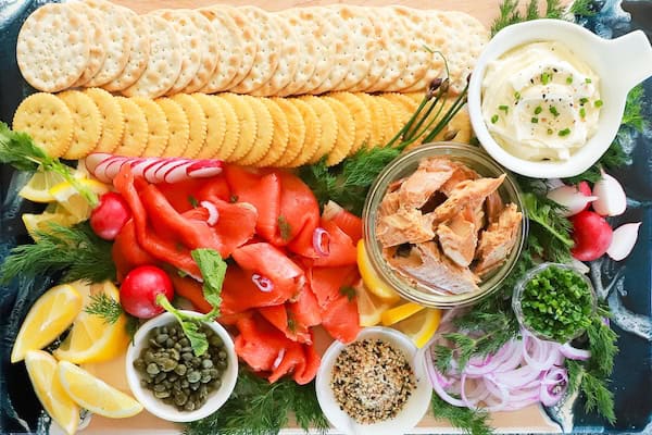 Smoked salmon crackers topped with cream cheese and dill on a festive white serving platter.
