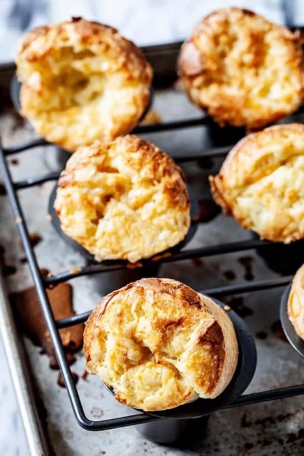 Golden cheese popovers cooling on a rack beside butter and holiday napkins.