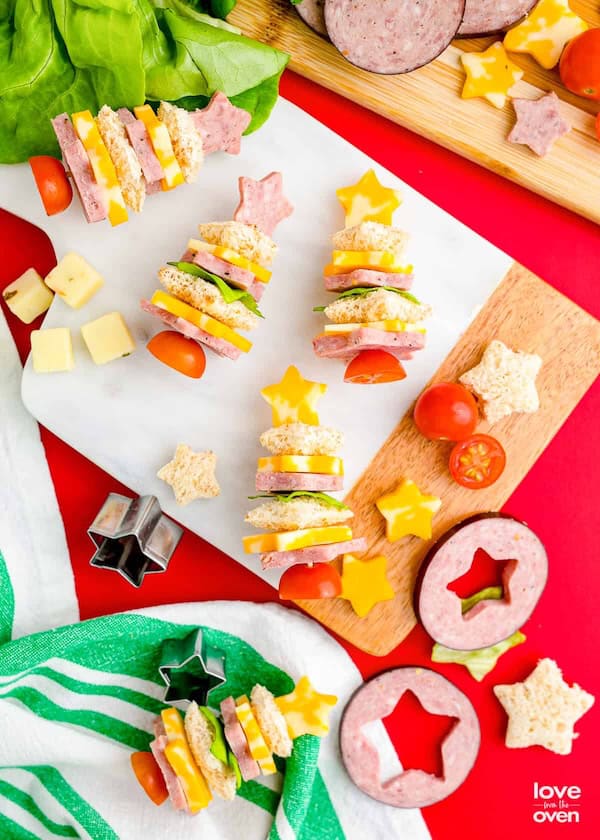 Assorted cute Christmas appetizers shaped like snowmen, trees, and wreaths on a holiday platter.