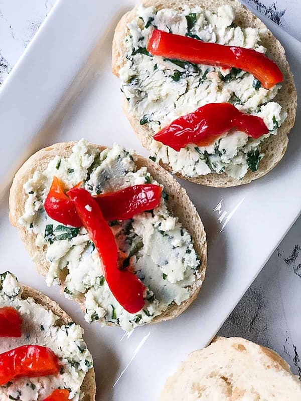 Bowl of feta red pepper dip garnished with herbs beside pita chips — festive appetizer spread.