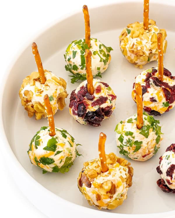 Mini cheese balls coated in herbs, nuts, and cranberries arranged on a white holiday plate.