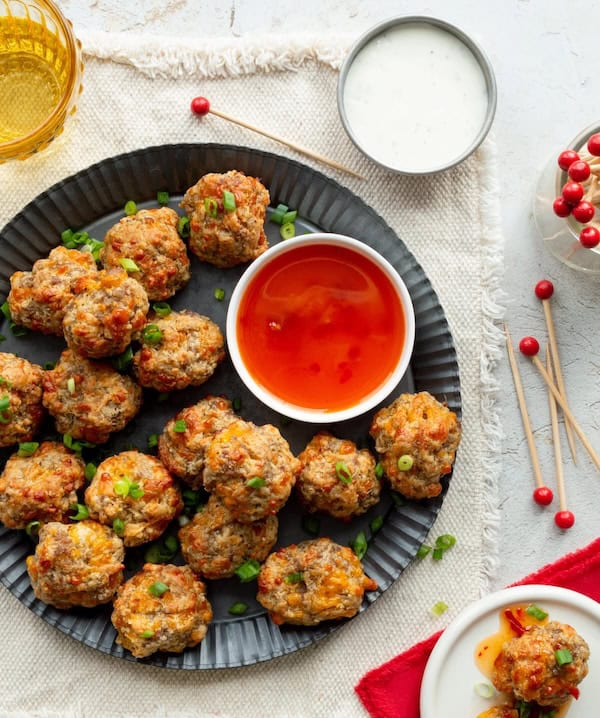 Cheddar cheese sausage balls stacked on a plate with dipping sauce on a red holiday napkin.
