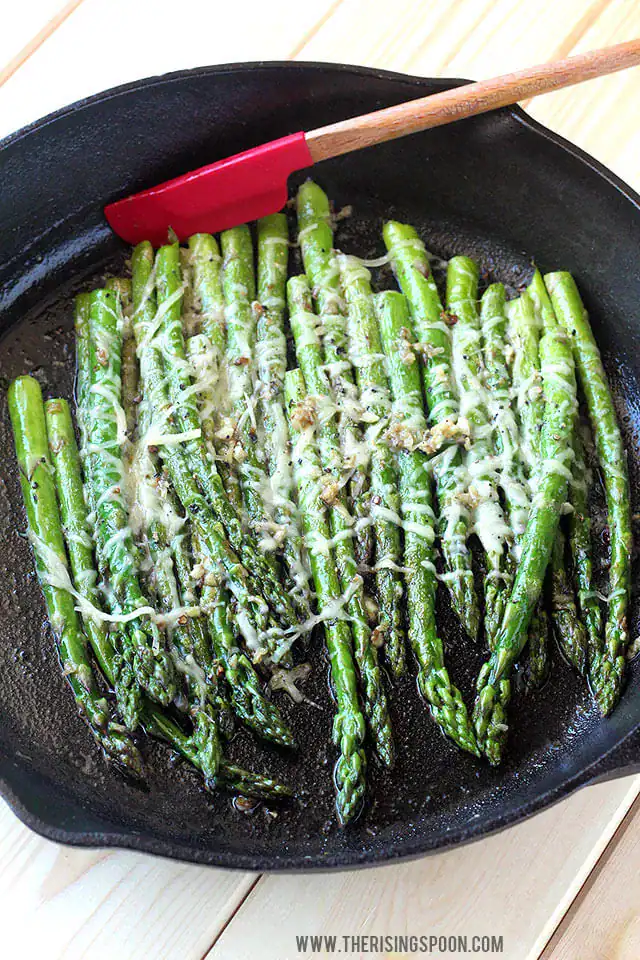 Sautéed asparagus with garlic, butter and melted Parmesan on a serving plate — vibrant easy Christmas side dish.