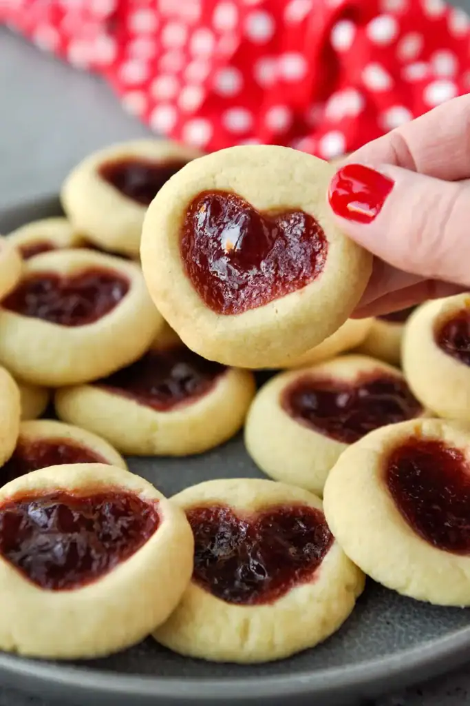 Heart-shaped jam cookies filled with red fruit jam on a baking tray