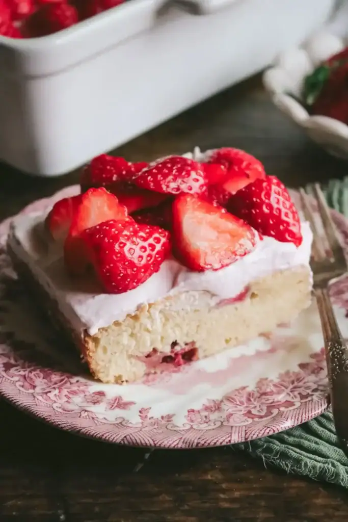 Strawberry snack cake topped with whipped cream and fresh strawberries on a plate